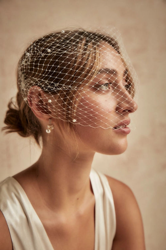 Woman wearing a birdcage veil against a neutral background