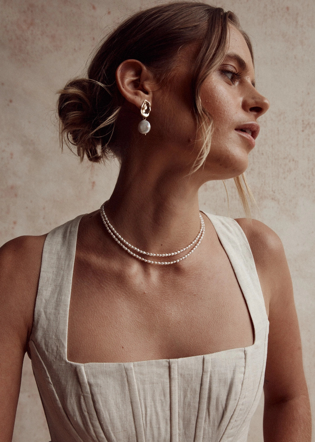 Woman wearing a pearl necklace and earrings against a neutral background