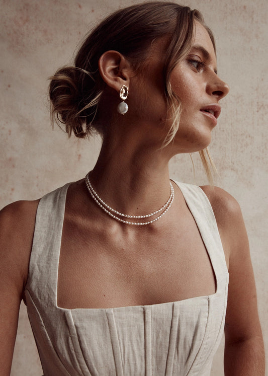 Woman wearing a pearl necklace and earrings against a neutral background
