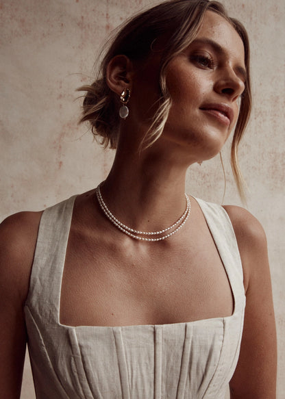 Woman wearing a pearl necklace and earrings against a neutral background
