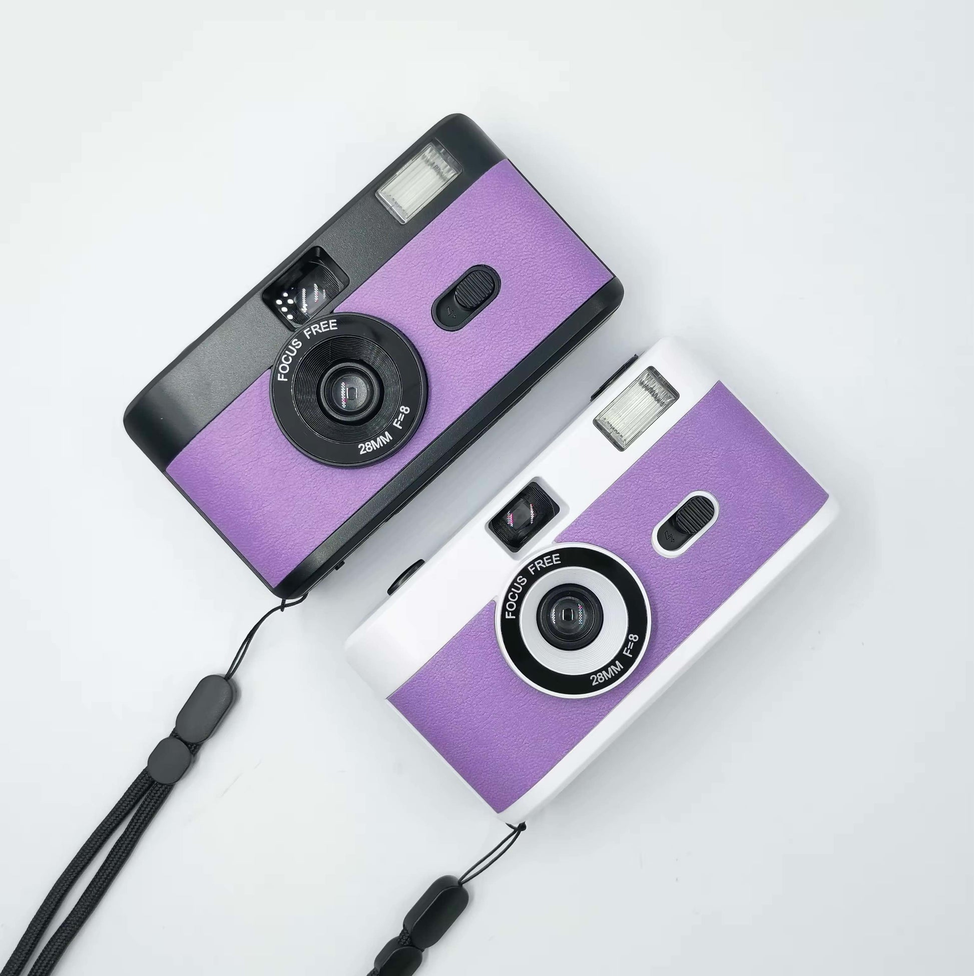 2 vintage looking film cameras a purple black one at the top and a silver purple at the bottom, aerial view one sits under the other. they are wedding accessory or favour