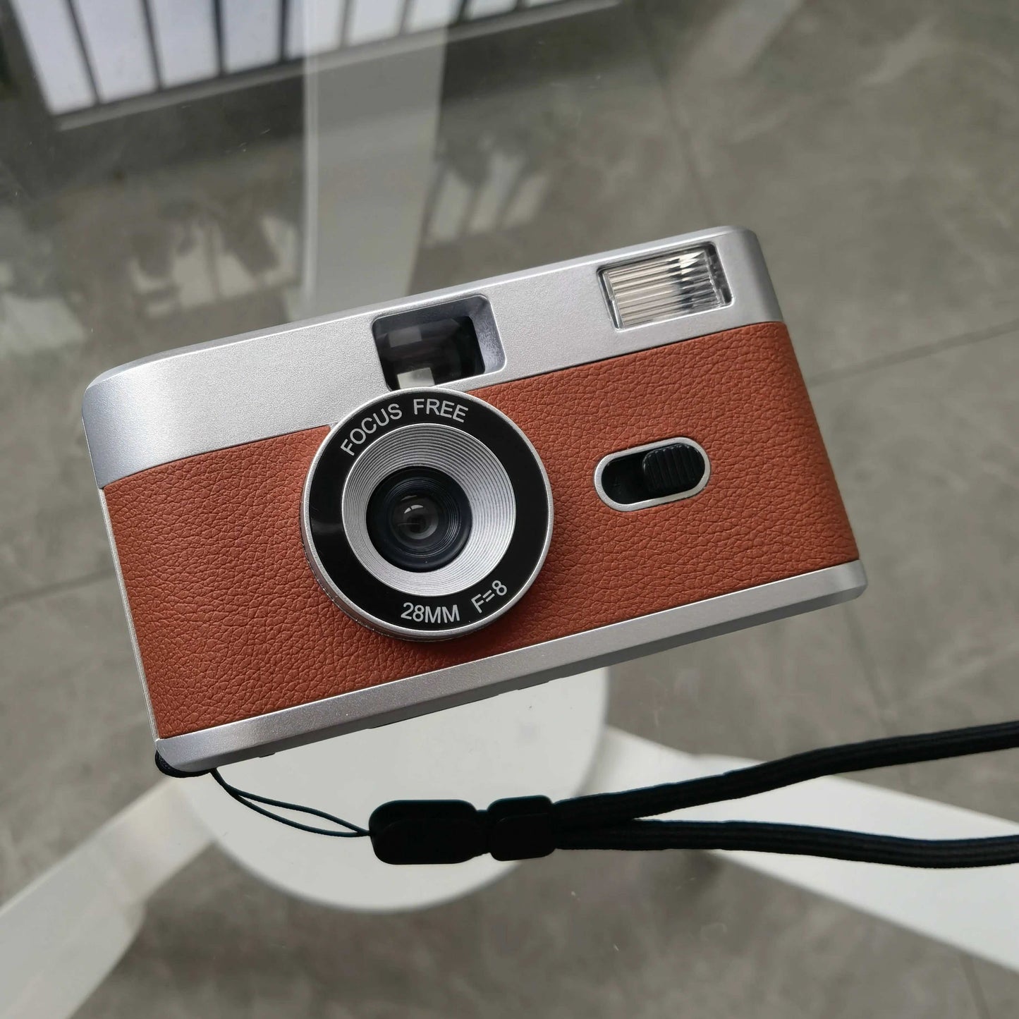 1 vintage looking film camera silver with a brown leather bottom half look. it sits on glass aerial view making a perfect wedding accessory
