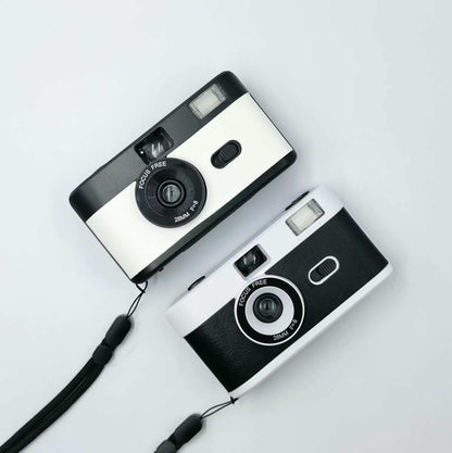 2 vintage looking film cameras a white on at the top and a black and white at the bottom, aerial view one sits under the other. 